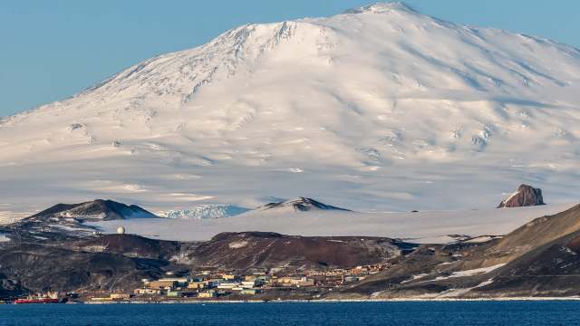 A snow-covered mountain with a research station and a body of water in the foreground.