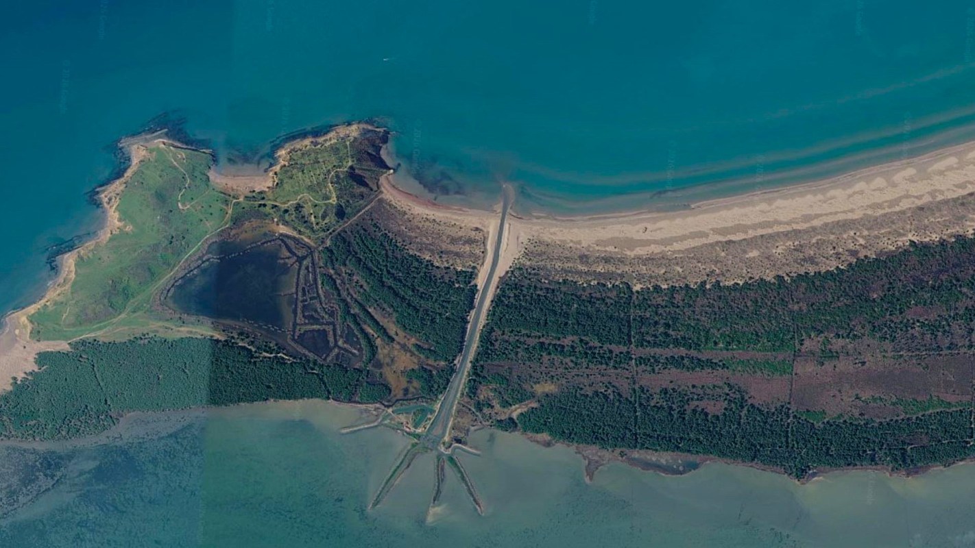 An aerial view of a coastal area featuring green land, sandy beaches, and intersecting waterways.