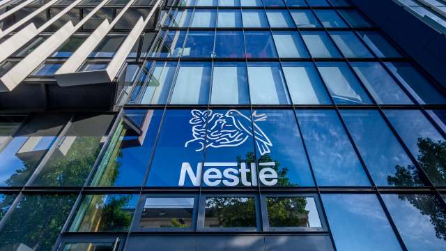 The Nestlé logo is prominently displayed on the glass facade of a modern building reflecting the sky and trees.