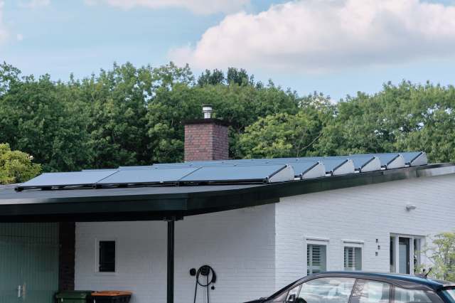 A house with solar panels on the roof, surrounded by greenery and featuring a visible brick chimney.