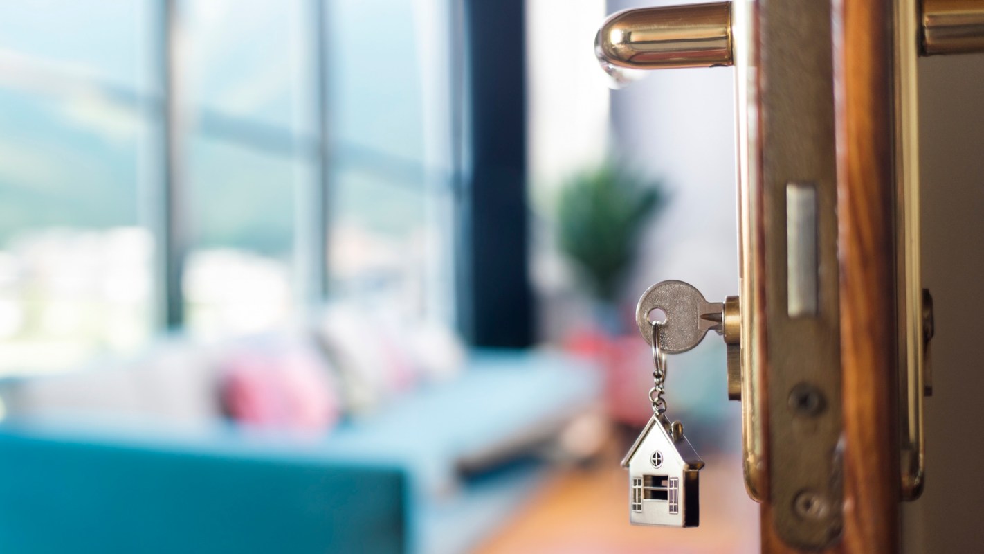 A key with a house-shaped keychain hangs from a door lock.