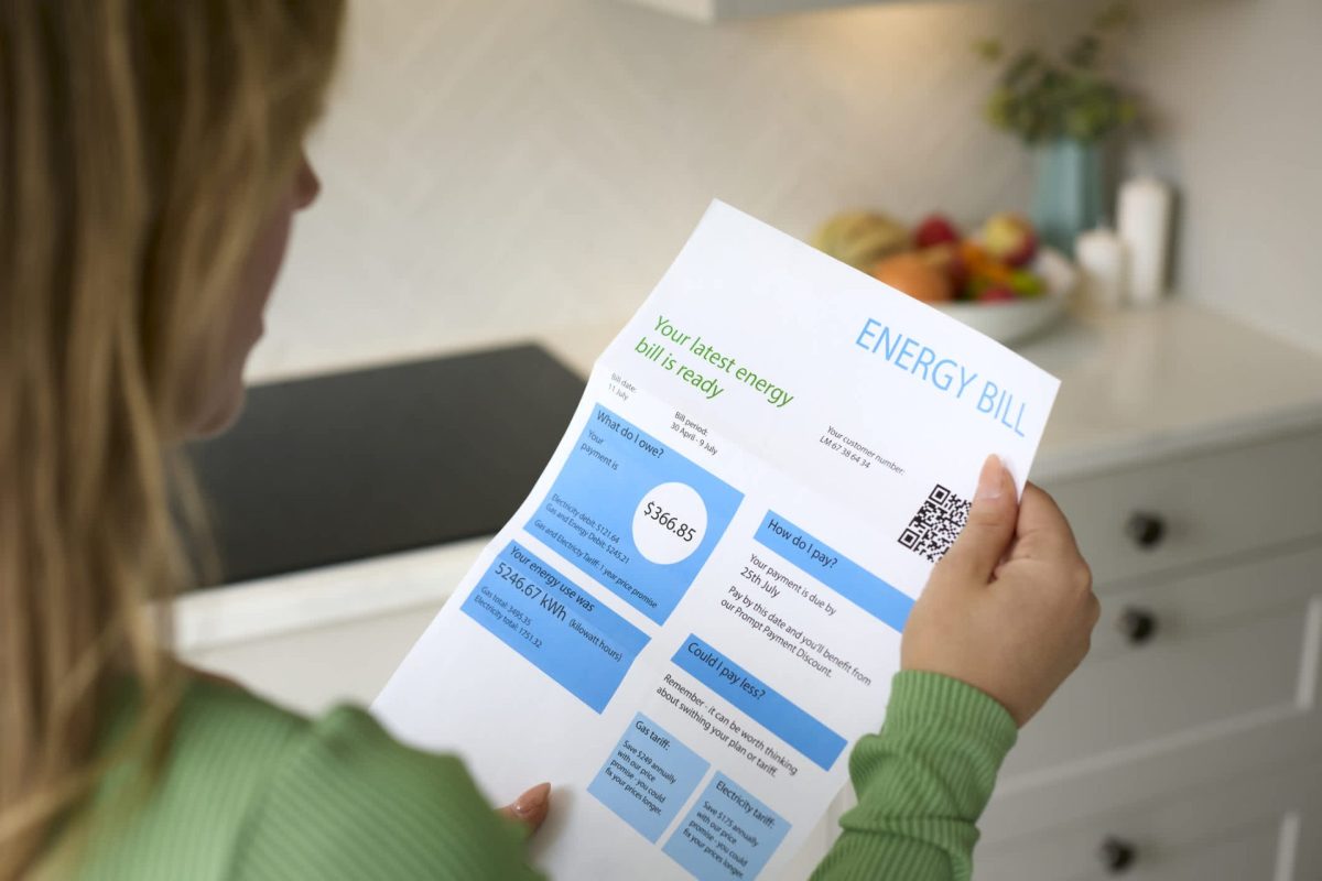 A person reviews their energy bill, detailing charges, usage, and payment options in a modern kitchen setting.