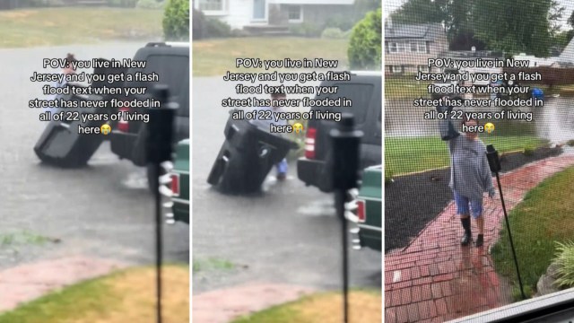 A person in rain gear struggling with a trash can in a flooded street.
