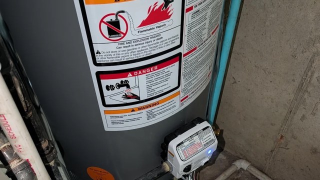 A water heater with safety warning labels and a digital control panel is displayed in a basement setting.
