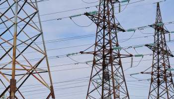 Three tall power transmission towers with power lines against a partly cloudy sky.