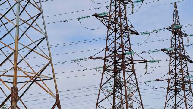 Three tall power transmission towers with power lines against a partly cloudy sky.