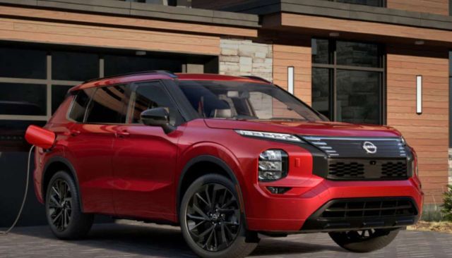 A bright red SUV is parked in front of a modern wooden home, with a charging cable connected to it.