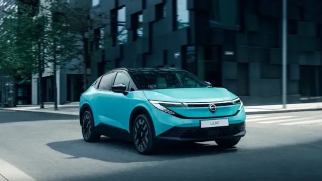A bright blue electric car driving on a city street with modern buildings in the background.