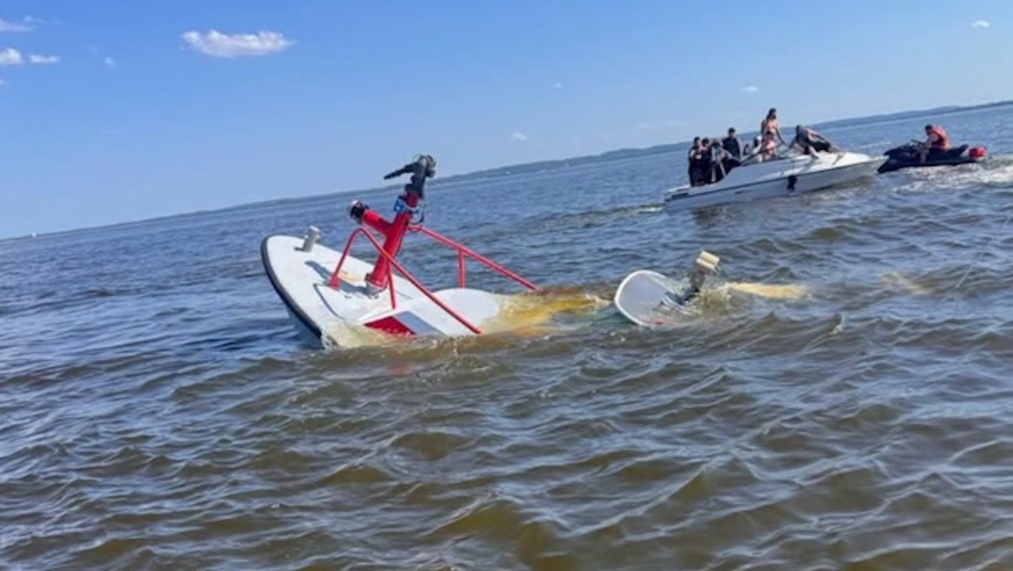 A partially submerged boat in water with other boats approaching to assist.