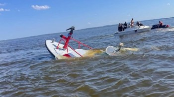 A partially submerged boat in water with other boats approaching to assist.