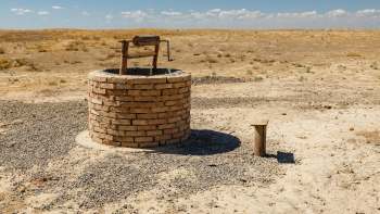 A brick well with a wooden handle stands in a dry, barren landscape under a clear blue sky.