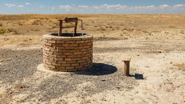 A brick well with a wooden handle stands in a dry, barren landscape under a clear blue sky.