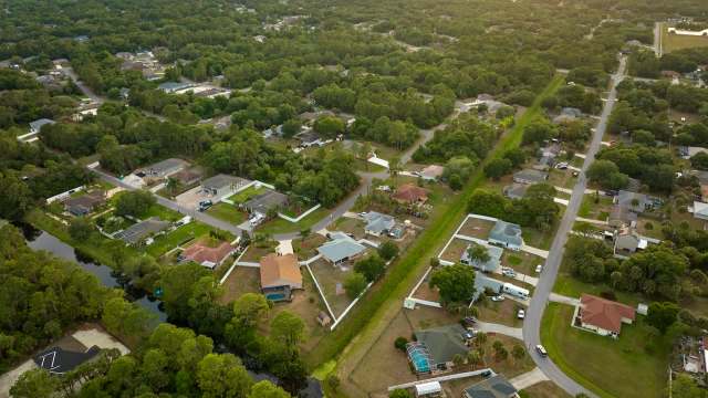 An aerial view of a neighborhood with houses, trees, a canal, and winding roads.