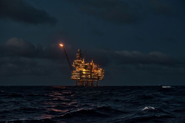 An oil rig stands in the ocean at night, with a flare.
