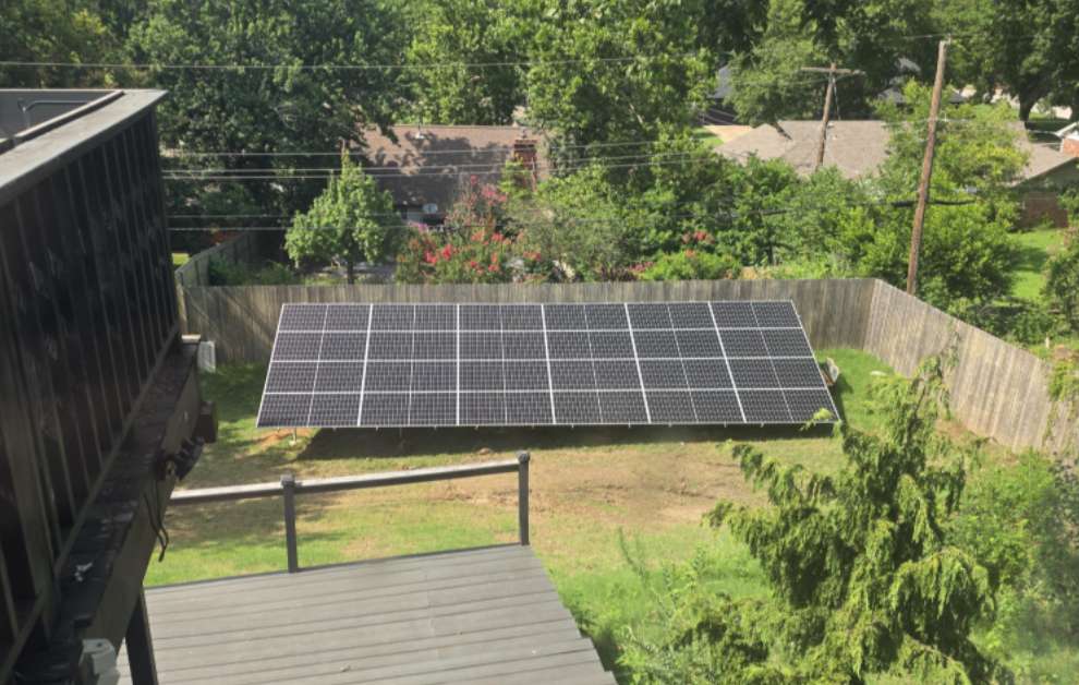 A solar panel installation in a backyard surrounded by trees and a wooden fence.