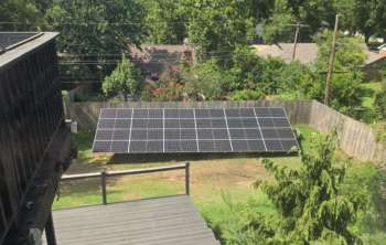 A solar panel installation in a backyard surrounded by trees and a wooden fence.