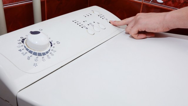 A person pressing the start button on a washing machine.