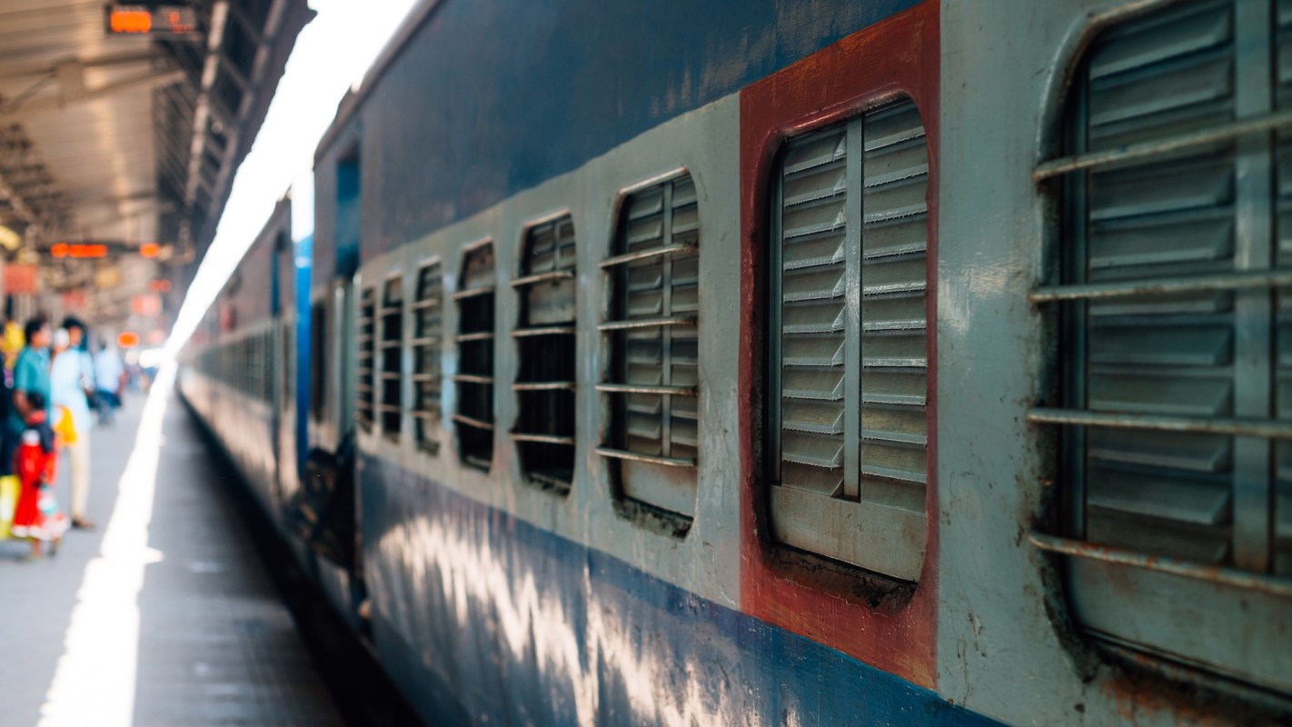 A close-up view of a weathered train with barred windows at a bustling train station.