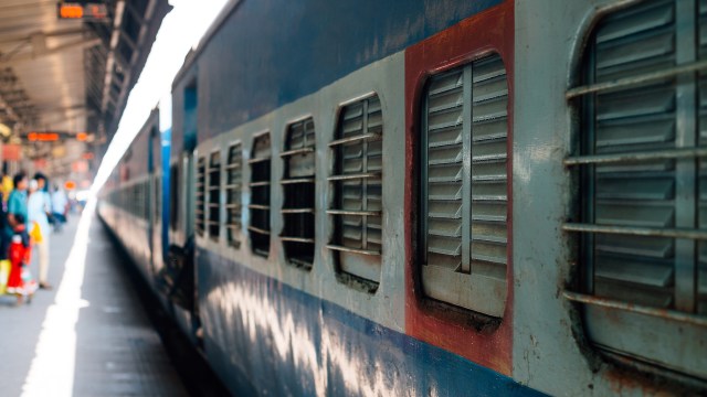 A close-up view of a weathered train with barred windows at a bustling train station.