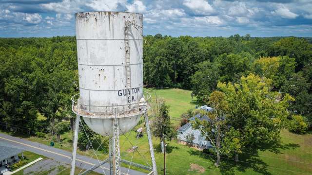 A water tower with the text "GUYTON GA" surrounded by green trees and a house nearby.