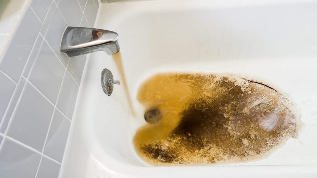 A bathtub filled with brown, murky water flowing from the faucet, revealing signs of dirt and staining.