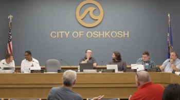 A city council meeting taking place in Oshkosh, with several members seated at a table.