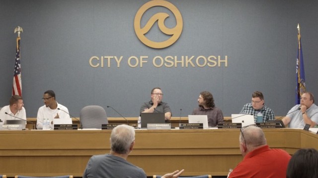 A city council meeting taking place in Oshkosh, with several members seated at a table.