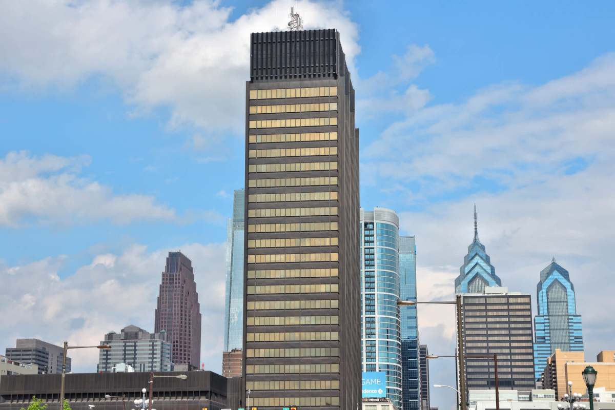 A skyline view featuring a tall dark building surrounded by modern architecture and a blue sky.