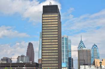 A skyline view featuring a tall dark building surrounded by modern architecture and a blue sky.