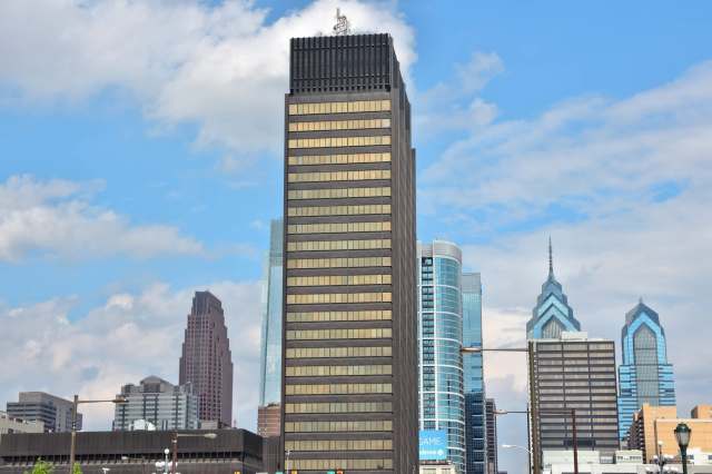 A skyline view featuring a tall dark building surrounded by modern architecture and a blue sky.