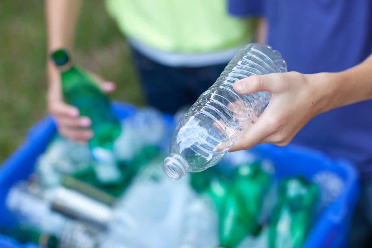 A person holds a clear plastic water bottle above a recycling bin filled with various bottles.