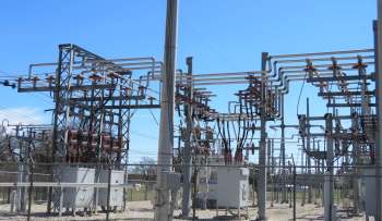 A power substation featuring metal structures, transformers, and power lines against a clear blue sky.