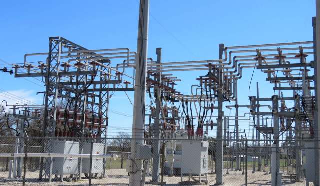 A power substation featuring metal structures, transformers, and power lines against a clear blue sky.