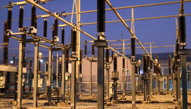 An electrical substation at dusk featuring tall structures with insulators and cables against a darkening sky.