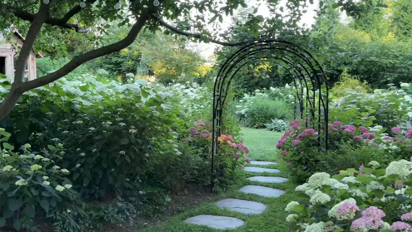 A stone garden path lined with flowers and leading through a metal archway.