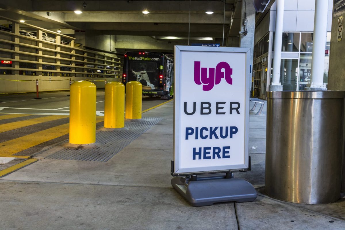 A sign indicating Uber and Lyft pickup locations at a parking area, with yellow bollards nearby.