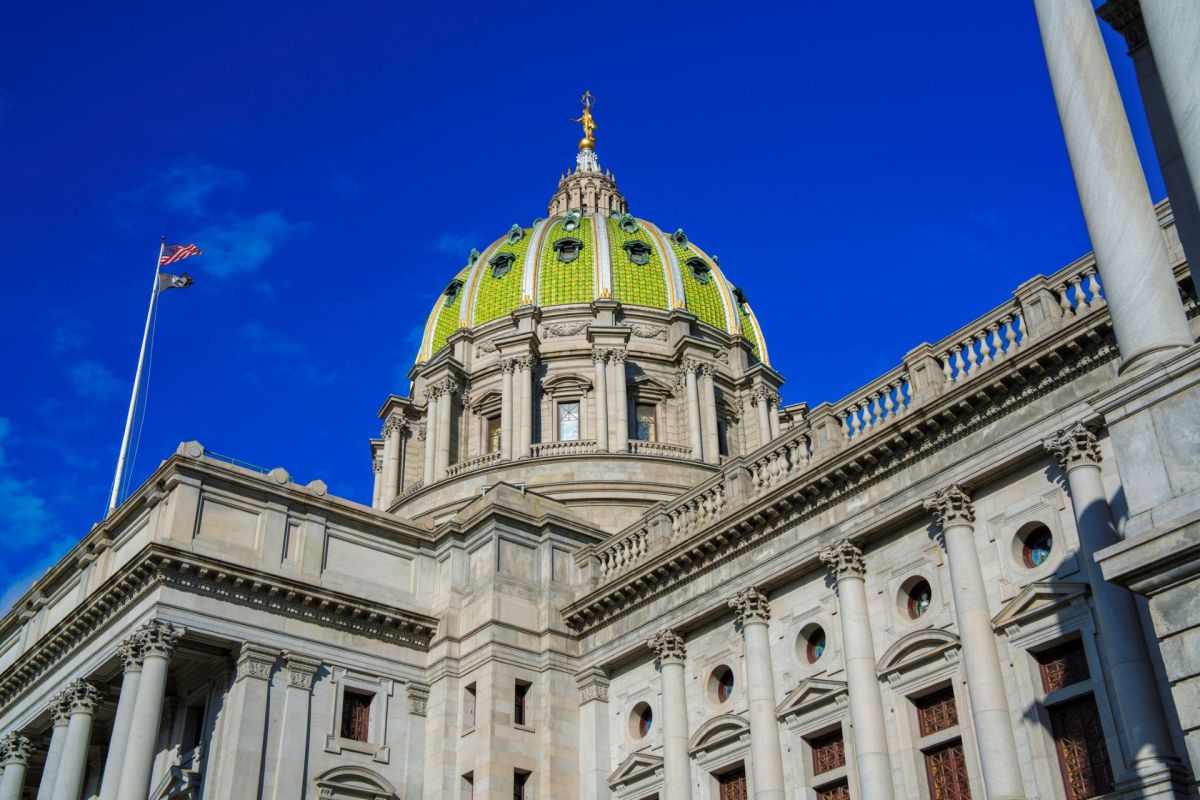 A close-up view of a grand building’s dome with a green and gold design against a clear blue sky.