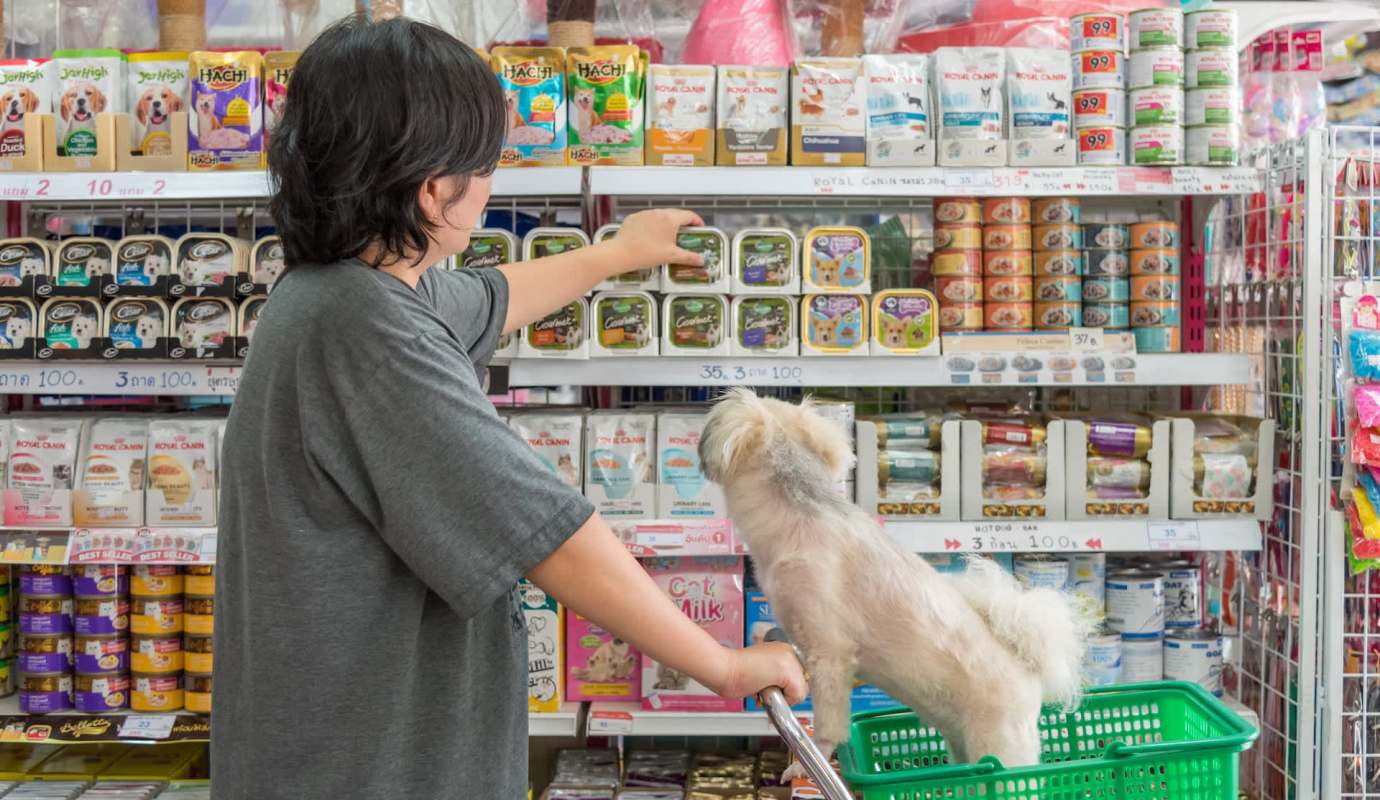 A person shopping for pet food with a dog.