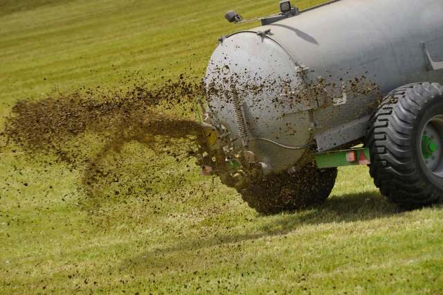 A tank vehicle releasing manure onto a field.