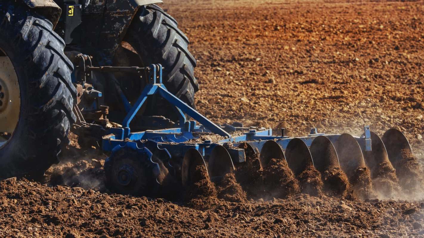 A tractor plowing a dry field with soil and dust being displaced.