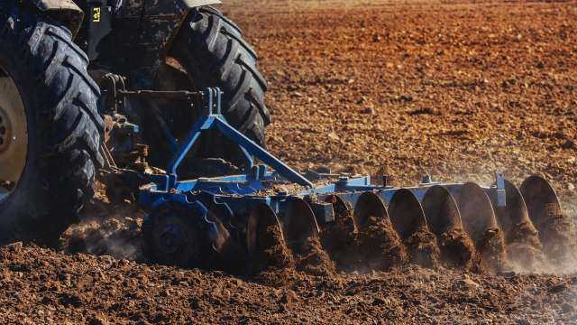 A tractor plowing a dry field with soil and dust being displaced.