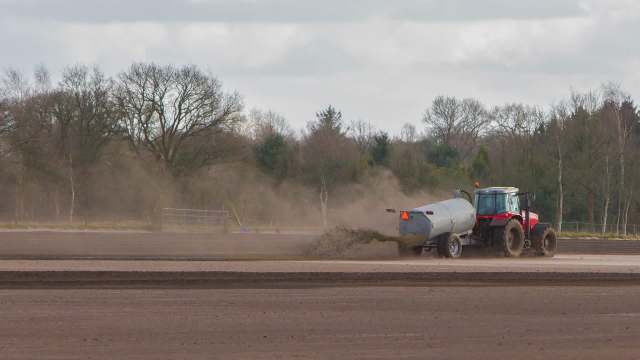 A red tractor fertilizing a field.