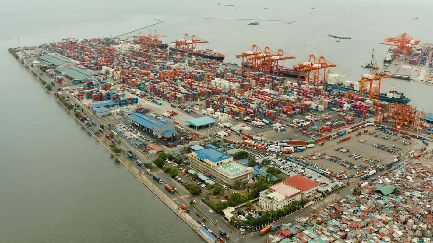 Aerial view of a busy port with numerous shipping containers and cranes along the waterfront.