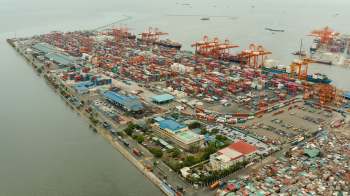 Aerial view of a busy port with numerous shipping containers and cranes along the waterfront.