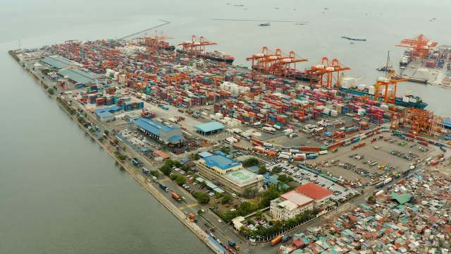 Aerial view of a busy port with numerous shipping containers and cranes along the waterfront.