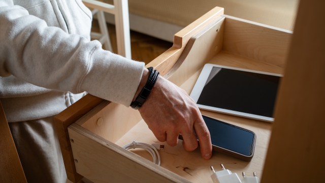 A person retrieving smartphone from a wooden drawer.