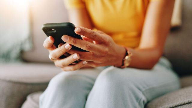 A person's hands holding a smartphone while sitting on a couch.