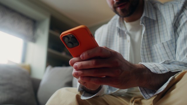 A man sitting on a couch, using an orange smartphone.