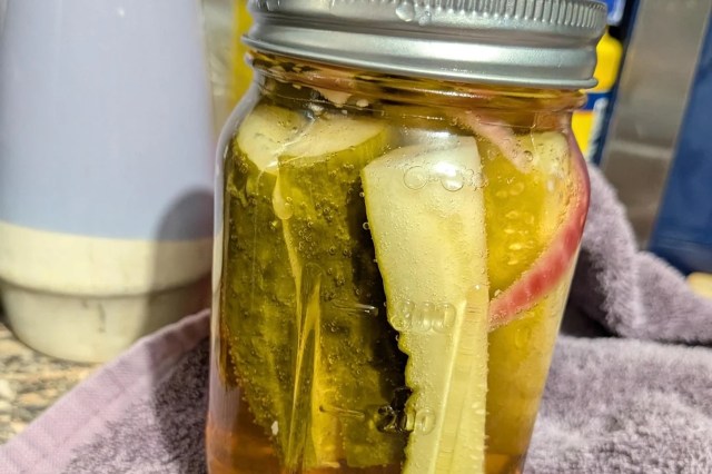 A jar filled with pickles and slices of onion submerged in liquid, resting on a cloth.