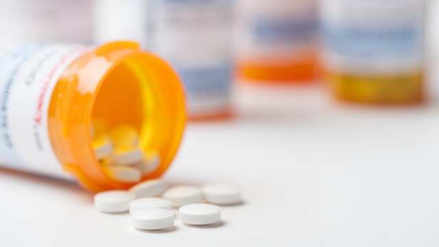 A prescription bottle tipped over, spilling white pills onto a white surface.
